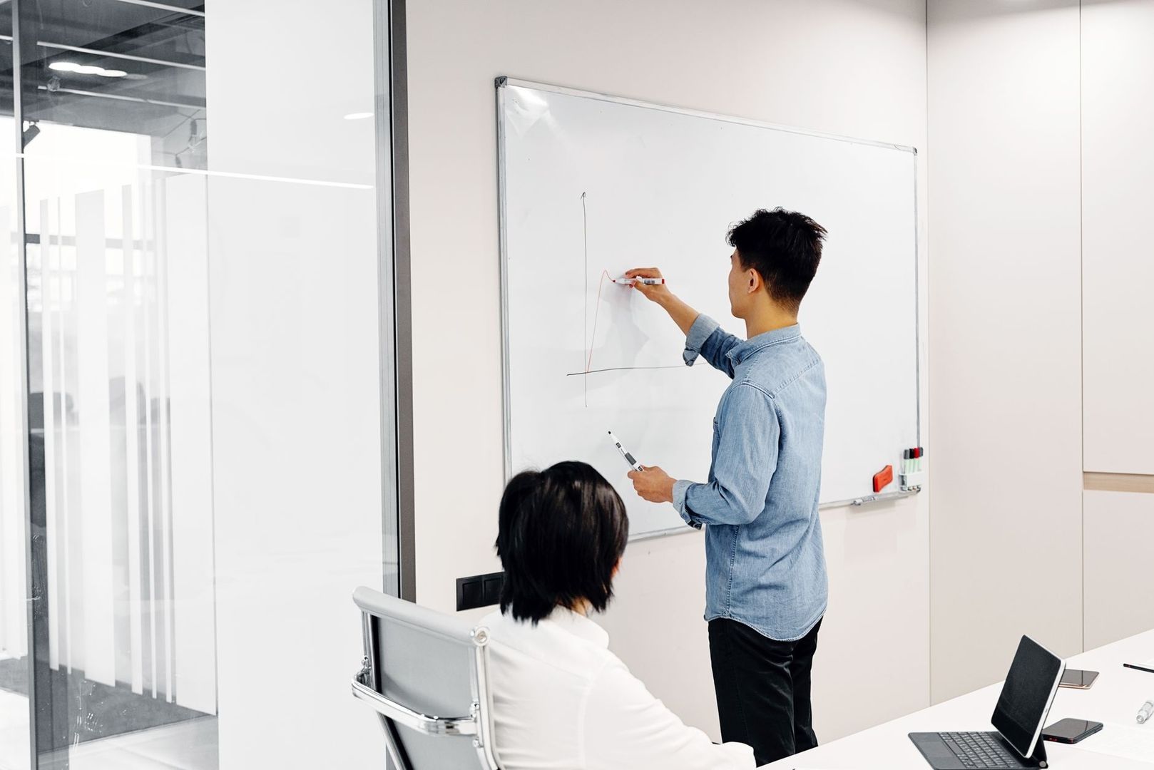 Zwei Personen besprechen eine ansteigende Kurve am Whiteboard